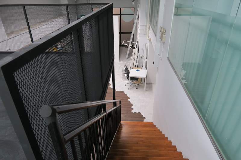 Looking down the timber-tread staircase from the loft, with a desk and green glass partition below - Steel loft platform with staircase in an industrial unit (Loft) | Wong Lye, BCA General Builder Class 2, Singapore