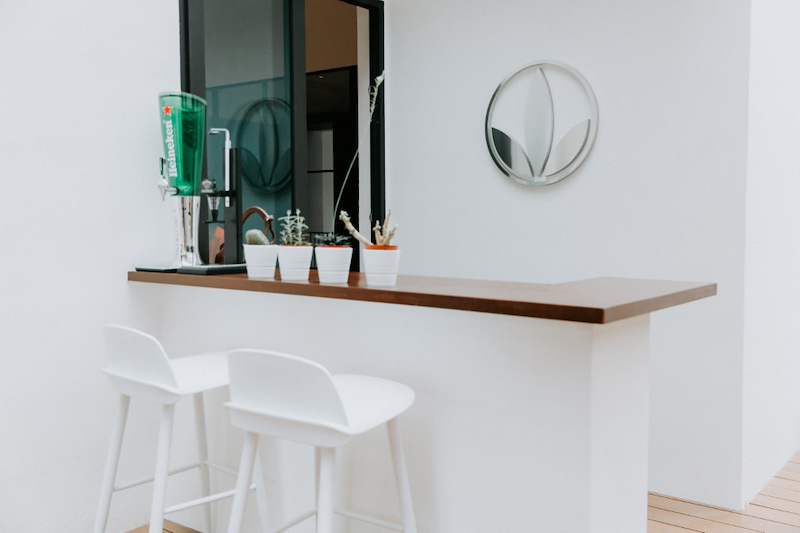Outdoor bar counter with a timber top, two white bar stools and a round mirror on a white wall - Landed house A&A with new facade, staircase and interiors (39EW) | Wong Lye, BCA General Builder Class 2, Singapore