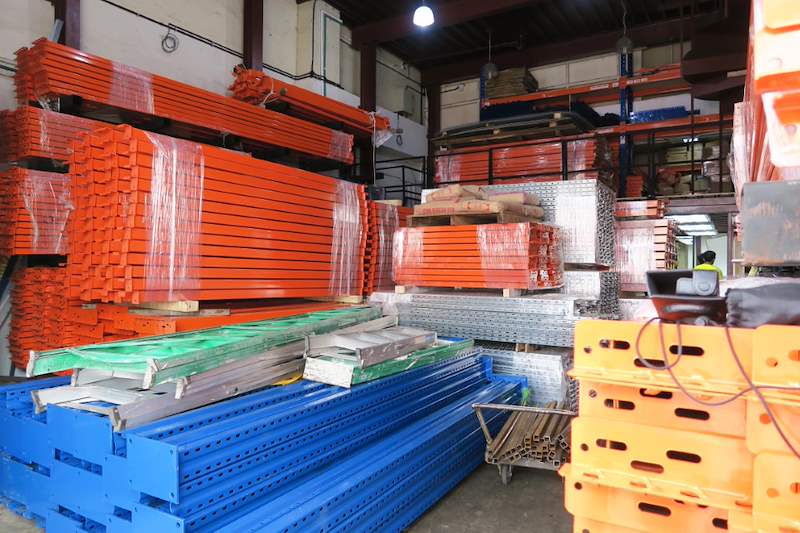 Bundles of orange racking beams and blue upright frames in the warehouse - Pallet racking beams and frames stacked in a warehouse (M12) | Wong Lye, BCA General Builder Class 2, Singapore