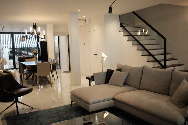 Open-plan living and dining with an L-shaped sofa, dining table and a black-framed staircase with timber treads - Terrace house A&A with new facade and full interior (3TBA) | Wong Lye, BCA General Builder Class 2, Singapore
