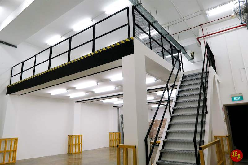 The mezzanine from below at an angle, showing the staircase and the hazard-striped edge - Steel mezzanine floor with staircase in a factory unit (OverseaFactory) | Wong Lye, BCA General Builder Class 2, Singapore