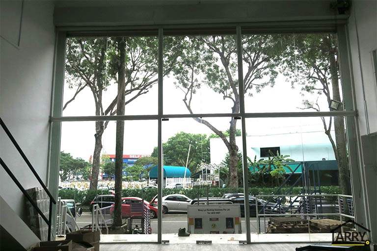 View through the glass frontage from inside towards the trees and road - Framed glass frontage and steel entrance stair for an industrial unit (M09) | Wong Lye, BCA General Builder Class 2, Singapore