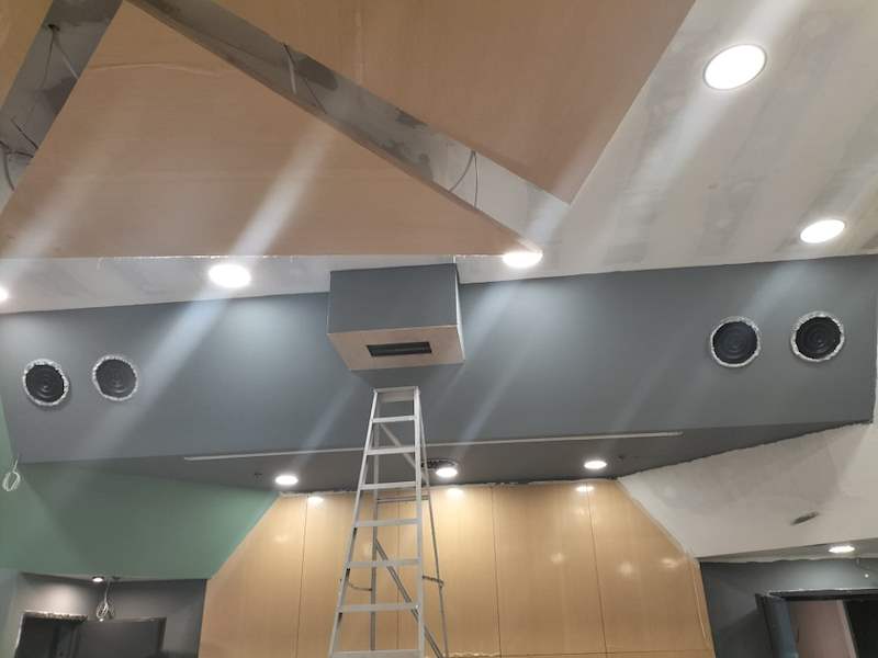 Angled ceiling panels being fitted around the speakers, ladder below - Music rehearsal studio fit-out with a faceted timber ceiling (Studio) | Wong Lye, BCA General Builder Class 2, Singapore