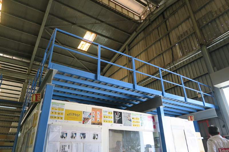 Blue steel mezzanine frame with railings above the shelving, under the factory roof - Steel mezzanine platform in a factory (M22) | Wong Lye, BCA General Builder Class 2, Singapore